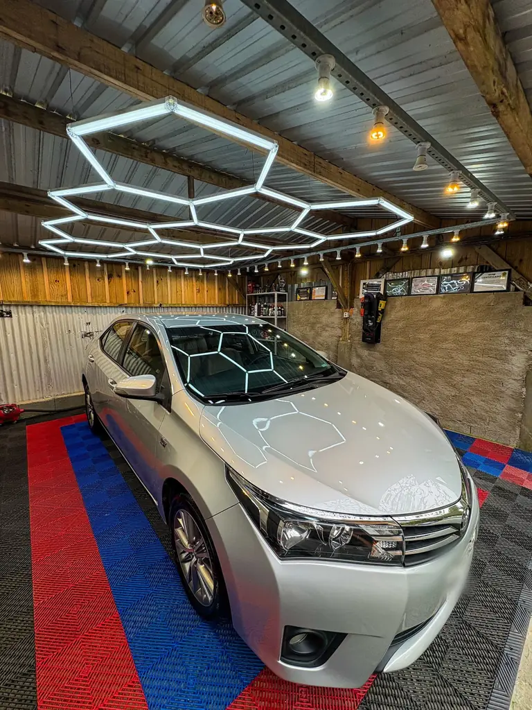 Corolla prata recém-polido sob o teto de luminárias hexagonais da GL, com a colmeia de luz refletida no capô e no para-brisa.